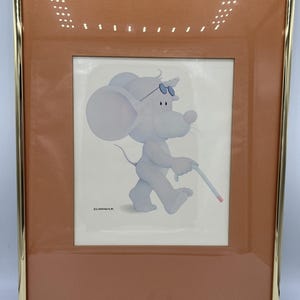 May include: Framed artwork featuring a cartoon mouse in sunglasses, walking and holding a cigarette. The artwork is in a gold frame with a rust-colored matting. The mouse is light blue and white, set against a white background.