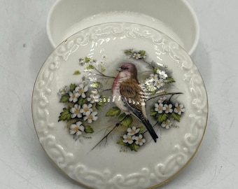 Caja redonda de porcelana vintage para joyas con borde de pergaminos en relieve y tapa con diseño floral de pájaros cantores.