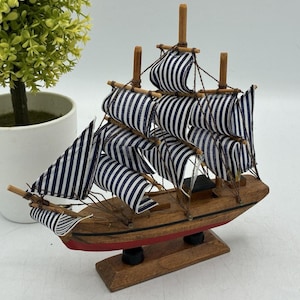May include: A wooden model sailboat with blue and white striped sails. The hull is brown with a red stripe along the bottom. The model sits on a wooden base and has several masts.