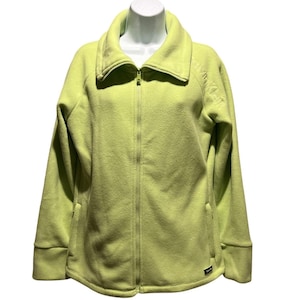 Puede incluir: Chaqueta de forro polar verde claro con cremallera y cuello alto. La chaqueta tiene mangas largas, una cremallera completa y el logotipo de Calvin Klein bordado en la manga superior izquierda. Una pequeña etiqueta de Calvin Klein está en la parte inferior derecha.