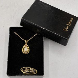 May include: A gold-tone necklace with a teardrop-shaped pendant featuring a central opal and a small ruby accent. The jewelry is presented in a black box labeled Van Doran with a gold tag reading GENUINE RUBY & OPAL inside the velvet-lined container.