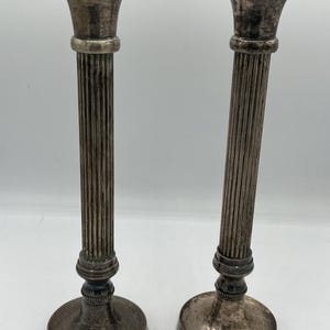 May include: A white ceramic mug with a black handle and the text "But First, Coffee" in a bold, black font. The mug is set against a blurred background, suggesting a cozy setting.