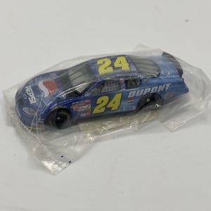 May include: A blue and black toy race car with the number 24 in yellow on the roof and side. The car has Pepsi and Dupont logos. The car is in a clear plastic package.