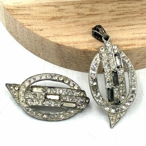 May include: A silver-toned brooch and a matching pendant, both featuring an oval frame encrusted with clear rhinestones and accented with rectangular baguette-cut stones arranged in a central horizontal or vertical bar pattern.