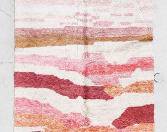May include: A rectangular rug with a textured, shaggy pile. The rug features horizontal stripes in shades of white, pink, and burgundy, with a fringed edge. The design has a watercolor effect, creating a soft, artistic look.