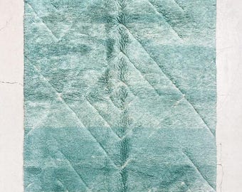 May include: A rectangular, turquoise rug with a geometric chevron pattern. The rug has a soft, plush texture and a fringe along the bottom edge. The rug is displayed on a white surface.