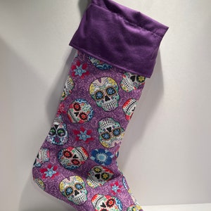 May include: Purple Christmas stocking with a colorful sugar skull pattern. The stocking has a purple cuff.