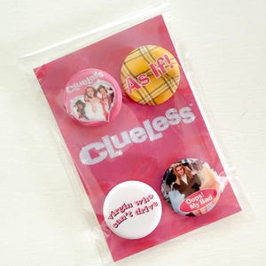 May include: A set of four Clueless-themed pinback buttons in a clear plastic bag. The buttons feature images and phrases from the movie, including "As If!" and "Virgin Who Can't Drive". The background is pink with the word "Clueless".