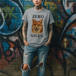 May include: A gray t-shirt with a fox graphic and the words "ZERO GIVEN" in black. The person is wearing ripped blue jeans and black boots. The background is a brick wall with graffiti.