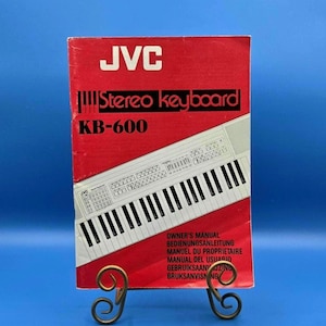 May include: A red JVC Stereo keyboard KB-600 owner's manual with white text and a black and white line drawing of the keyboard on the cover. The manual includes the text: JVC Stereo keyboard KB-600 OWNER'S MANUAL BEDIENUNGSANLEITUNG MANUEL DU PROPRIETAIRE.