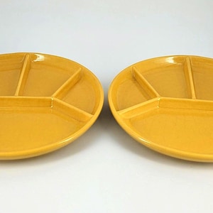 May include: Two oval-shaped, divided serving dishes. Each dish is a solid, glossy yellow color and has five compartments. The plates are designed for serving appetizers, snacks, or condiments. The dishes are made of ceramic or a similar material.