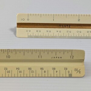May include: Two off-white triangular architectural scales with brown center grooves. The top scale features the text 'LUTZ' and markings from 0 to 10. The bottom scale displays markings from 8 to 12 and the text 'JAPAN' with a 3/32 scale indicator.
