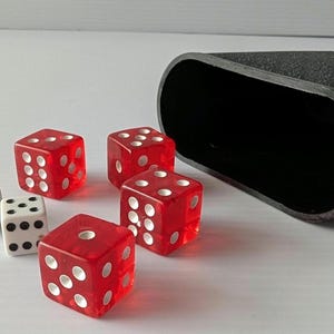May include: A set of six-sided dice including four translucent red dice with white pips and two opaque white dice with black pips, accompanied by a black, oval-shaped dice cup with a textured exterior and a hollow interior for storage.