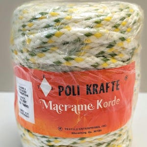 May include: A spool of macrame cord wrapped in clear plastic. The cord is white with yellow and green diamond-shaped accents. The label reads "POLI KRAFTE Macrame Korde" and "TEXTILE ENTERPRISES, INC."