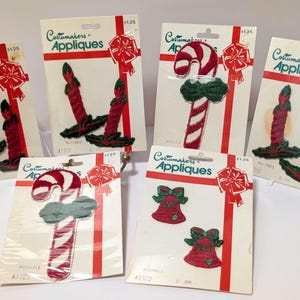 May include: Several Christmas-themed appliques on cards. Designs include red candles, candy canes, and bells with green accents. Each card has the text "Costumakers Appliques" and a red ribbon design.