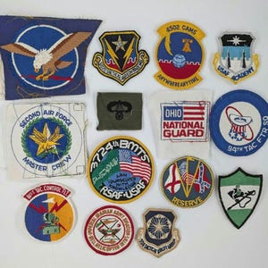 May include: A collection of embroidered military patches, featuring various designs and colors. The patches include eagles, stars, flags, and text such as "USAF Academy", "Ohio National Guard", and "Second Air Force Master Crew".