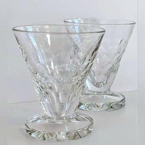 May include: Two clear, stemmed dessert glasses. The glasses have a flared bowl with a textured, diamond-like pattern and a round base. The glasses are made of clear glass and are set against a white background.