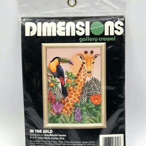 May include: A Dimensions Gallery Crewel embroidery kit titled In The Wild, featuring a toucan and a giraffe in a jungle setting. The packaging displays the 5" x 7" frame size, includes Persian wool yarn, cotton thread, and printed fabric.