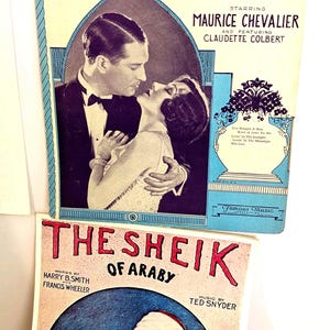 May include: Vintage sheet music covers. The top cover features a couple from "The Big Pond" starring Maurice Chevalier and Claudette Colbert. The bottom cover is for "The Sheik of Araby". Both covers have text and illustrations.