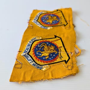 May include: Two yellow fabric patches with embroidered emblems. Each patch features a blue and red circular design with a gold figure and the text "452 D TACTICAL AIRLIFT WING". The patches have frayed edges.