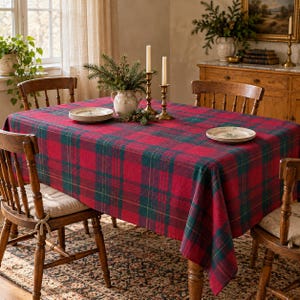 May include: A rectangular tablecloth featuring a red and dark green plaid pattern. The fabric covers a wooden table surrounded by four wooden chairs. Two white ceramic plates are placed on the surface, along with a white vase containing greenery.
