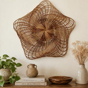May include: A star-shaped wall hanging crafted from woven brown rattan reeds, featuring a swirling, concentric pattern that radiates from the centre. The structure is open and airy, showcasing the natural texture and varied brown tones of the material.