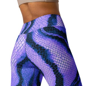 Puede incluir: Primer plano de leggings morados y azules con estampado de piel de serpiente. Los leggings son de cintura alta y están hechos de un material elástico. El diseño presenta un patrón de escamas repetido en tonos morados, azules y negros.