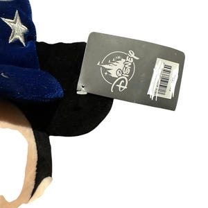 May include: A plush Mickey Mouse ear headband with a blue velvet wizard hat featuring silver stars. A Disney tag is attached to the headband.