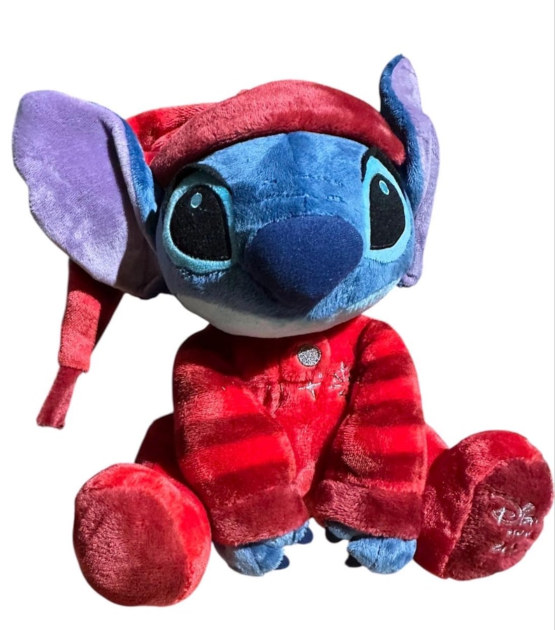 May include: A plush toy of the character Stitch, featuring blue fur, large purple-lined ears, and a dark blue nose. The character wears a red nightcap and matching red pajamas with horizontal stripes, a silver button, and a small embroidered star.