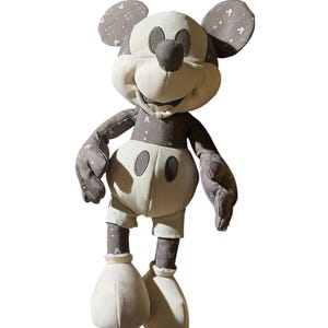 Puede incluir: Un mu&ntilde;eco de peluche de Mickey Mouse de estilo vintage. El mu&ntilde;eco presenta una cara, manos y pies de color crema, con orejas, brazos y piernas grises. Las secciones grises tienen un sutil patr&oacute;n de estrellas blancas. El mu&ntilde;eco lleva pantalones cortos color crema.