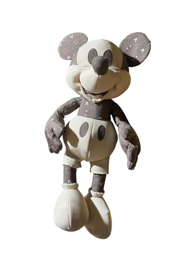 Puede incluir: Un mu&ntilde;eco de peluche de Mickey Mouse de estilo vintage. El mu&ntilde;eco presenta una cara, manos y pies de color crema, con orejas, brazos y piernas grises. Las secciones grises tienen un sutil patr&oacute;n de estrellas blancas. El mu&ntilde;eco lleva pantalones cortos color crema.