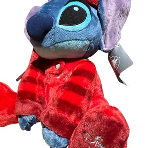 May include: A blue plush character with large ears wearing a red striped pajama set and a matching red cap. The character has a dark blue nose and large black eyes. A silver Disney Store 2024 logo is embroidered on the bottom of the left foot.