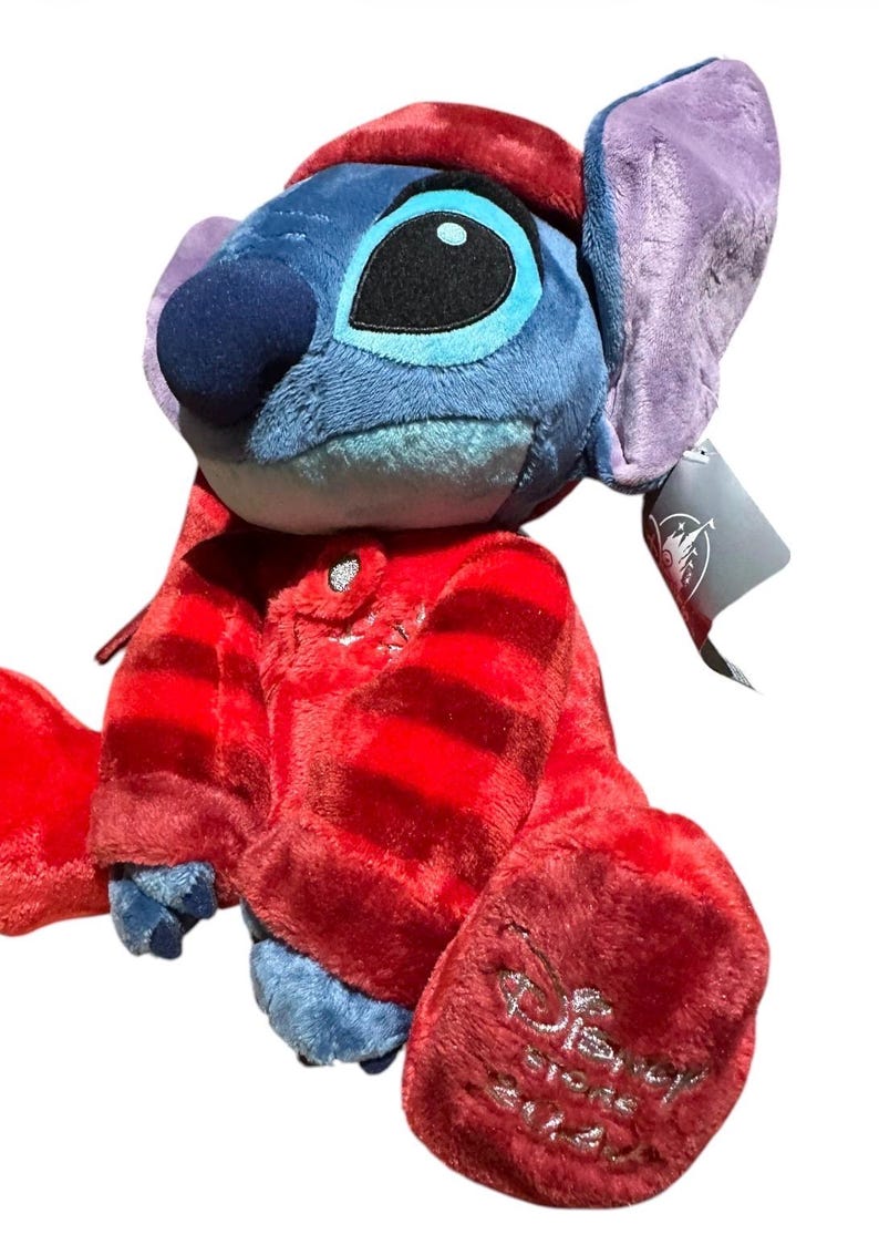 May include: A blue plush character with large ears wearing a red striped pajama set and a matching red cap. The character has a dark blue nose and large black eyes. A silver Disney Store 2024 logo is embroidered on the bottom of the left foot.