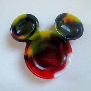 以下が含まれることがあります： カラフルなミッキーマウス型の樹脂製皿。赤、白、黄、緑、黒の鮮やかなミックスが特徴です。耳は濃い色合いで、ボウルは光沢のある仕上がりです。小物入れに最適です。