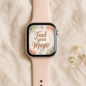 以下が含まれることがあります： ペールピンクのスマートウォッチと、お揃いのバンド。文字盤には「Find your Magic」の文字が装飾的な書体で表示され、花柄や天体のグラフィックで囲まれています。時計はニュートラルな背景に置かれています。