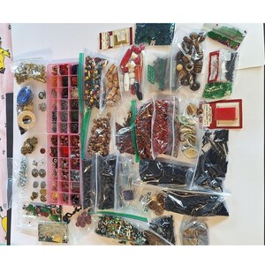May include: A collection of craft supplies, including beads, buttons, and sequins, organized in clear plastic bags and a pink divided container. Various colors and shapes are visible, with some items still in their original packaging.