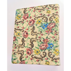 May include: A rectangular, floral-patterned item with a beige background. The design features red, pink, blue, and yellow flowers, along with brown decorative elements. The item appears to be a book or a similar rectangular object.
