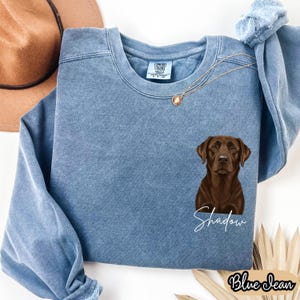 May include: A blue jean-colored sweatshirt featuring a brown Labrador Retriever graphic with the name "Shadow" in white script. The sweatshirt has a crew neck and long sleeves. The words "Blue Jean" are printed in a script font at the bottom.