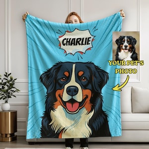 May include: A light blue blanket featuring a cartoon illustration of a Bernese Mountain Dog with the name "Charlie" in a speech bubble. A photo of the dog is shown next to the blanket. The blanket has a comic book style design.
