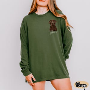 May include: Olive green long-sleeve shirt featuring a brown Labrador Retriever illustration with the name "Shadow" in a cursive font. The shirt is made of a soft material and has a relaxed fit. The word "Hemp" is in a small oval at the bottom right.