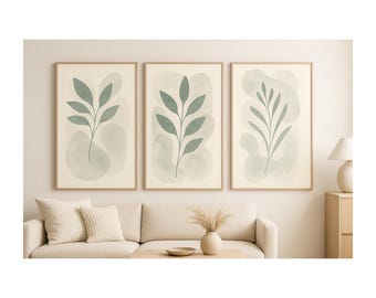 May include: Three framed botanical art prints. Each print features a green leaf design on a cream background with a light green watercolor wash. The frames are a light wood color. The prints are displayed above a cream-colored sofa.