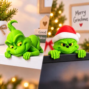 May include: Two green character figurines. One figure is lying flat with a tuft of hair, yellow eyes, and a wide grin. The second figure wears a red and white Santa hat, has yellow eyes, and is positioned over the edge of a black screen.