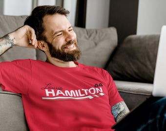 May include: A red t-shirt with the text "Lewis Hamilton" in white and red, and the number "44". The shirt has a white and red stripe design. The person is smiling and wearing the shirt.
