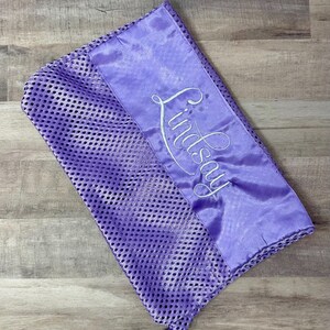 May include: A lavender mesh laundry bag with a satin panel embroidered with the name "Lindsay" in white script. The bag has a drawstring closure and is designed for delicate items.