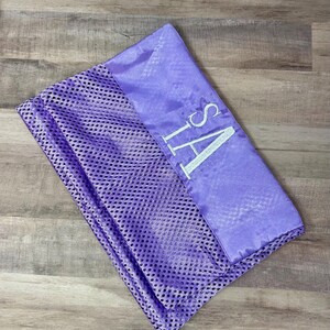 May include: A lavender mesh laundry bag with a satin top section. The top section is embroidered with the letters "SA" in white. The bag is closed with a drawstring.