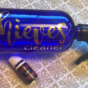 May include: A blue glass spray bottle with a black spray nozzle. The bottle has a gold label that says "Thieves Cleaner". A small bottle of Thieves essential oil is also pictured.
