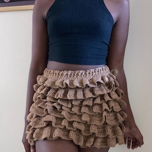 May include: A black halter top paired with a brown crochet skirt. The skirt features multiple layers of ruffled crochet, creating a textured and voluminous look. The outfit is a combination of casual and bohemian styles.