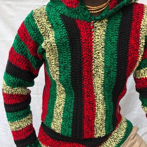 May include: A handmade crochet hoodie in a striped pattern of red, green, black, and yellow. The hoodie features a hood and long sleeves. The garment is made of thick yarn, giving it a textured appearance. The overall style is casual and comfortable.