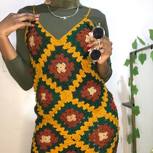 Puede incluir: Vestido de crochet hecho a mano con un diseño de patchwork vibrante. El vestido presenta un cuello en V y tirantes finos. La paleta de colores incluye tonos de amarillo, verde, marrón y beige. El vestido es de un estilo bohemio único.