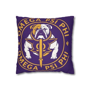May include: Square purple pillow featuring a gold and white bulldog illustration. The design includes the words "OMEGA PSI PHI" in a gold circular pattern around the bulldog and a gold symbol. The pillow is a decorative item.